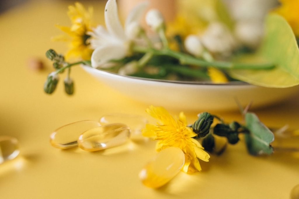 yellow-and-white-flowers-on-white-ceramic-bowl-7526020 Close-up of herbal capsules and flowers on a yellow background, natural wellness theme.